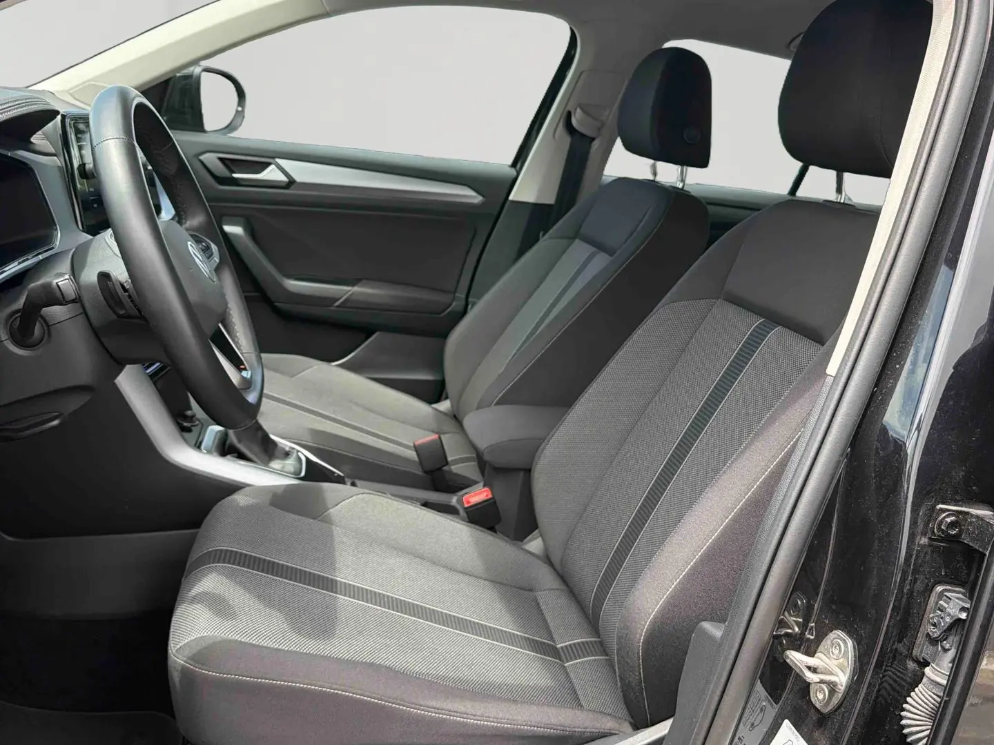 Vue intérieure côté gauche du Volkswagen T-Roc noir 2025, montrant les sièges avant en tissu gris et la console centrale.