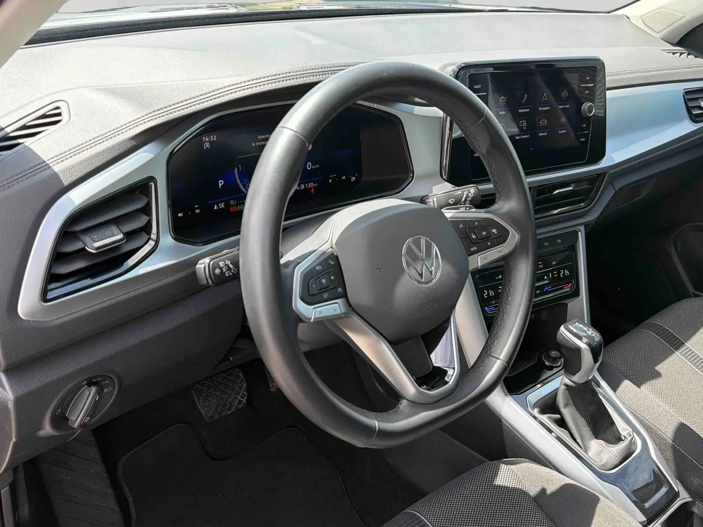 Vue intérieure centrée sur le volant cuir multifonctions et la console centrale du Volkswagen T-Roc 2025 noir avec boîte manuelle.