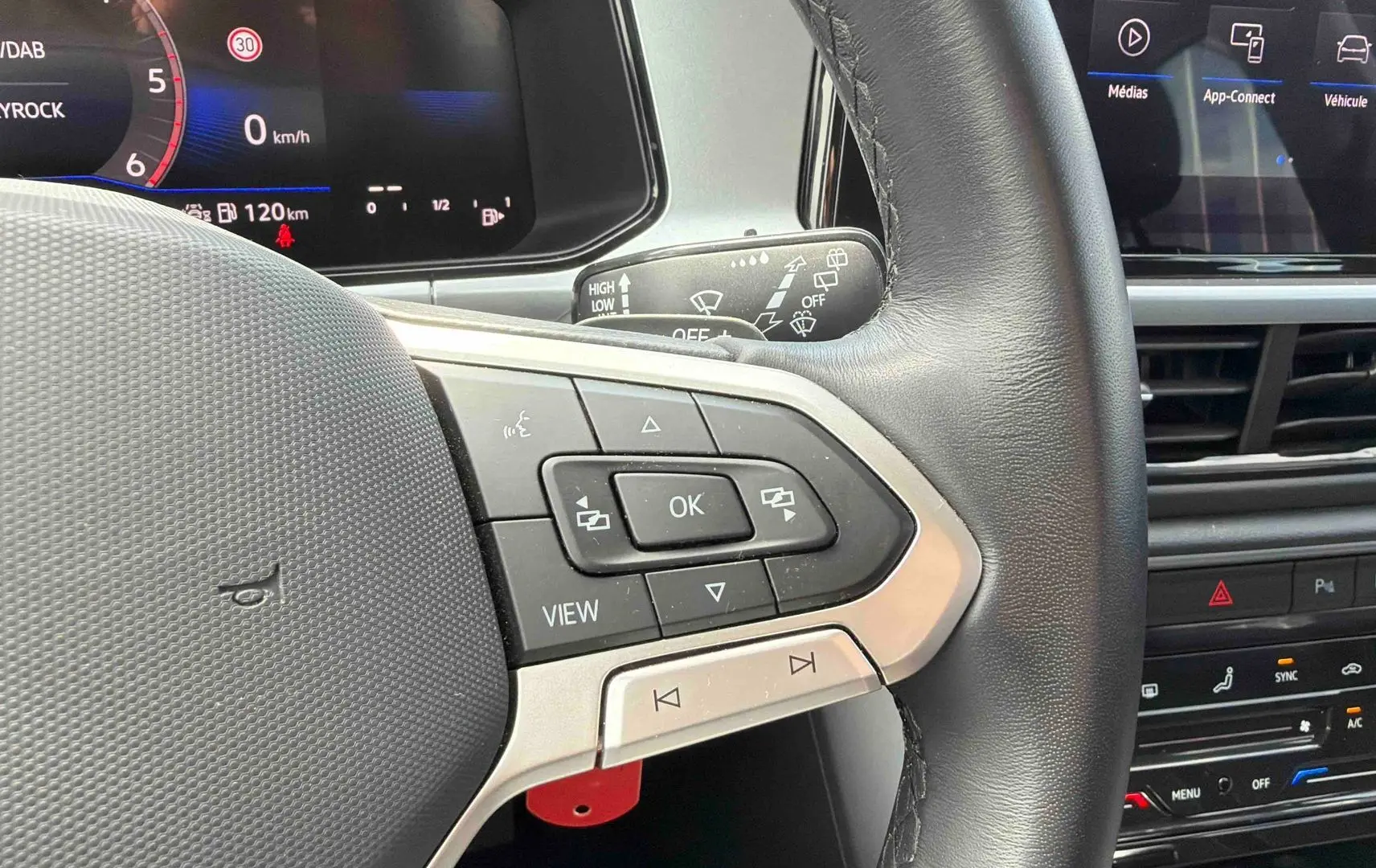 Gros plan sur le volant cuir multifonctions côté gauche du Volkswagen T-Roc noir avec tableau de bord digital et écran tactile.