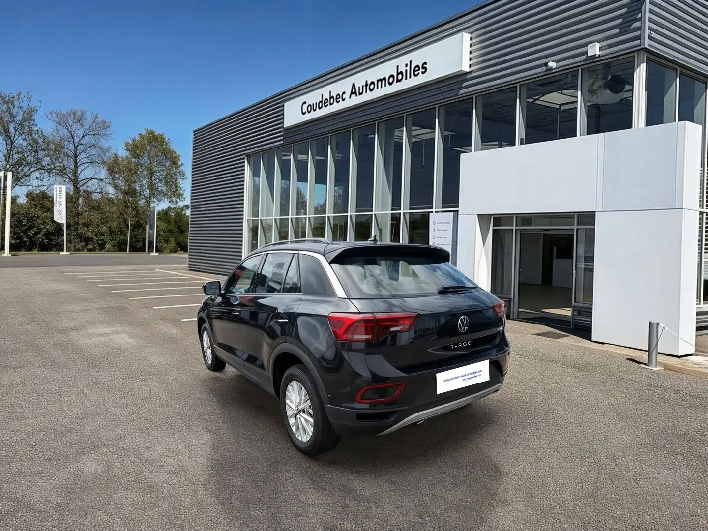 Vue 3/4 arrière droite d'un Volkswagen T-Roc noir 2025 stationné devant un bâtiment moderne de concession.