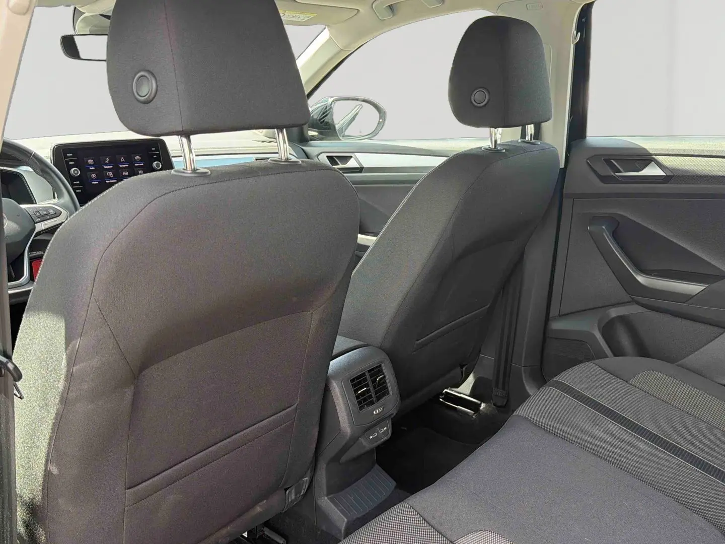 Vue intérieure arrière du Volkswagen T-Roc noir 2025, montrant les sièges avant, la console centrale avec aérateurs et port USB.