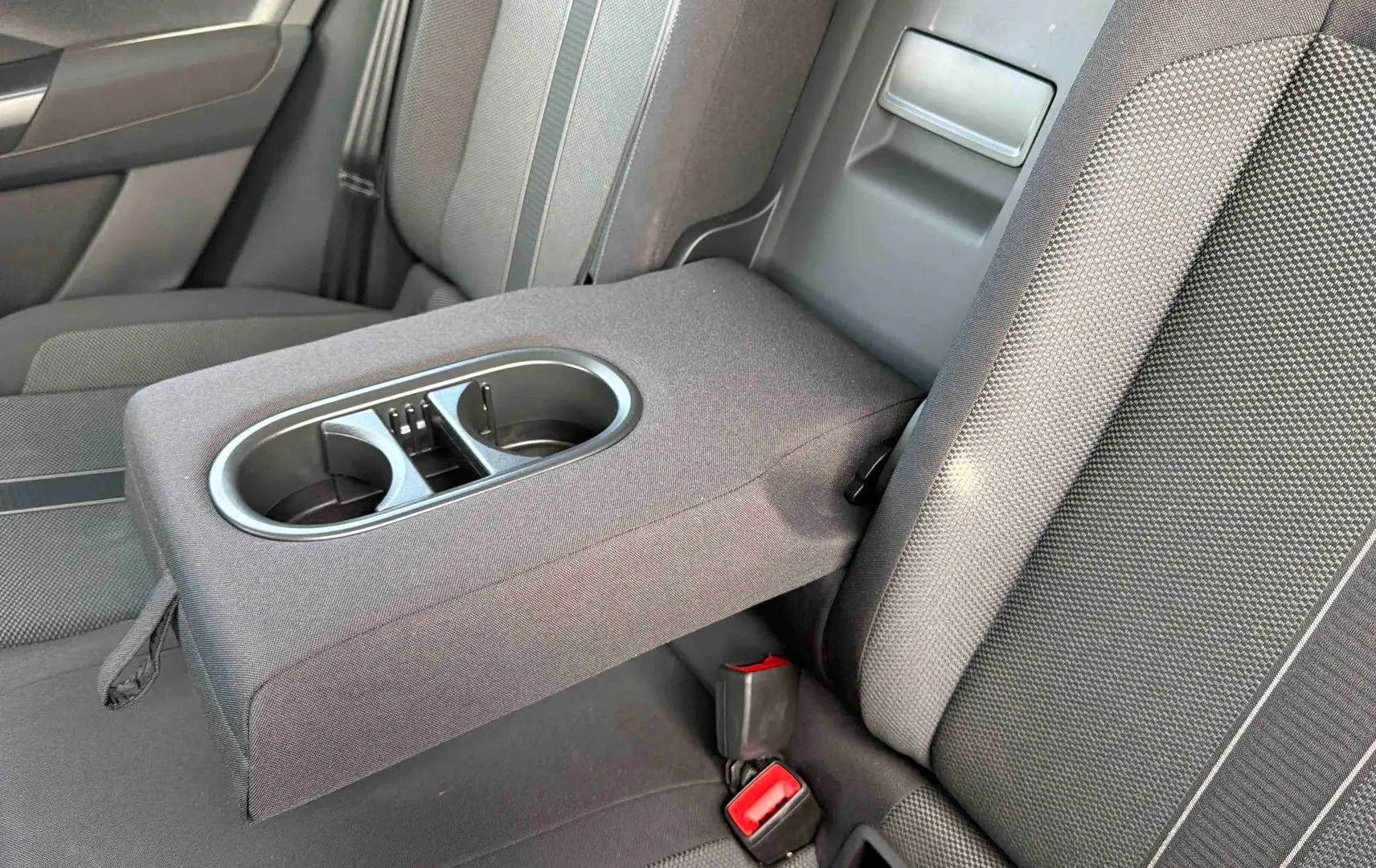 Vue rapprochée de l'accoudoir central arrière avec porte-gobelets sur les sièges tissu gris du Volkswagen T-Roc noir.