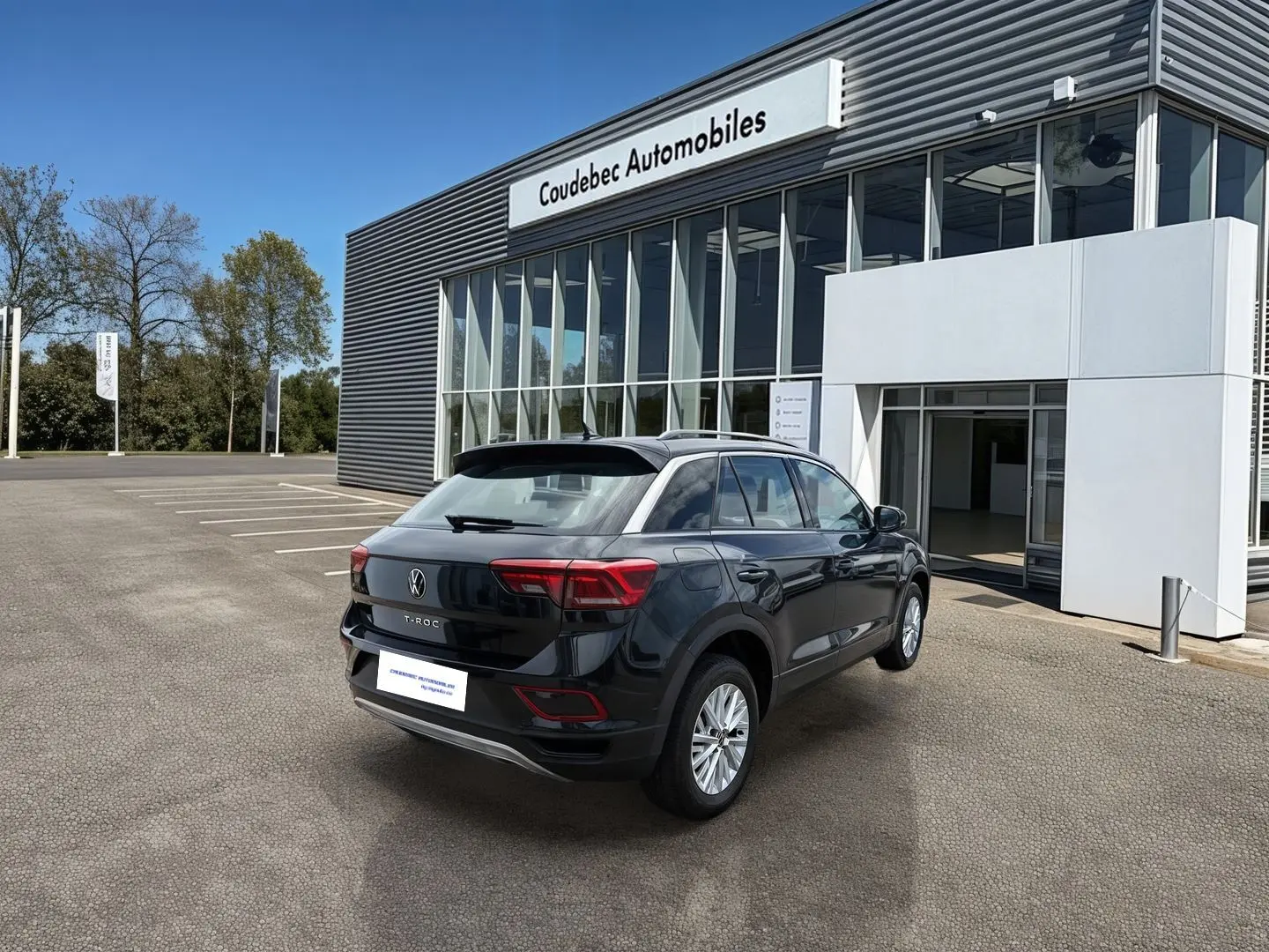 Vue 3/4 arrière droite d'un Volkswagen T-Roc noir stationné devant un bâtiment commercial moderne.