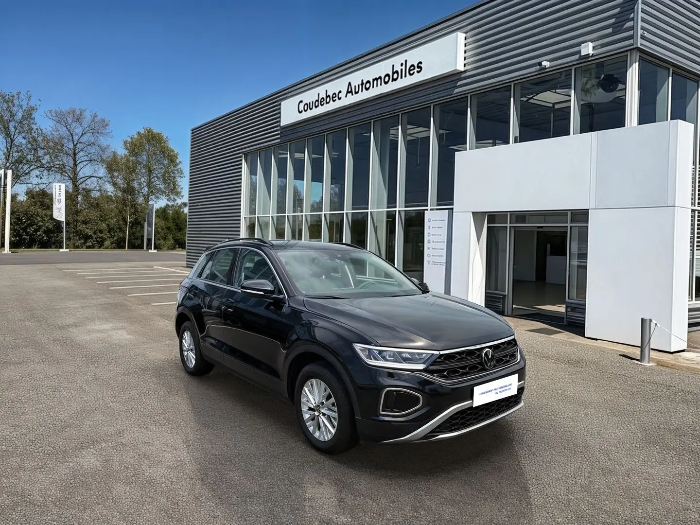Volkswagen T-Roc noir vue 3/4 avant droit, avec jantes alliage 16'' et calandre distinctive, devant un concessionnaire.
