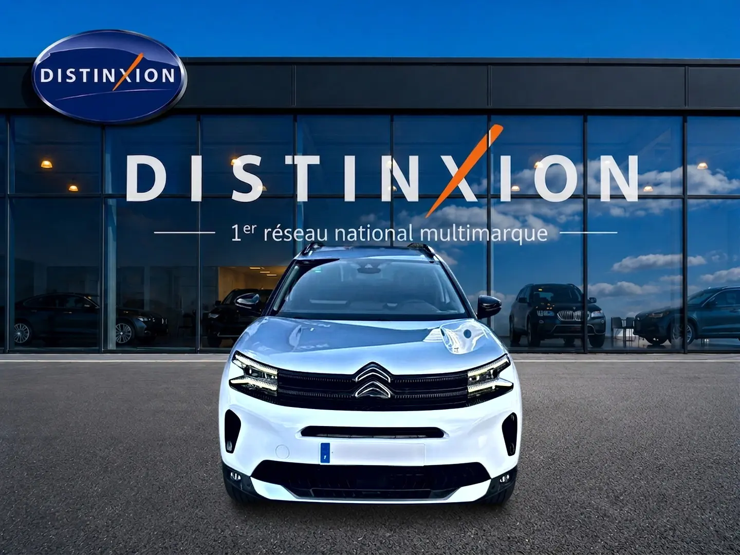Vue frontale d'un Citroën C5 Aircross blanc 2025 garé devant une vitrine avec logo Distinxion.