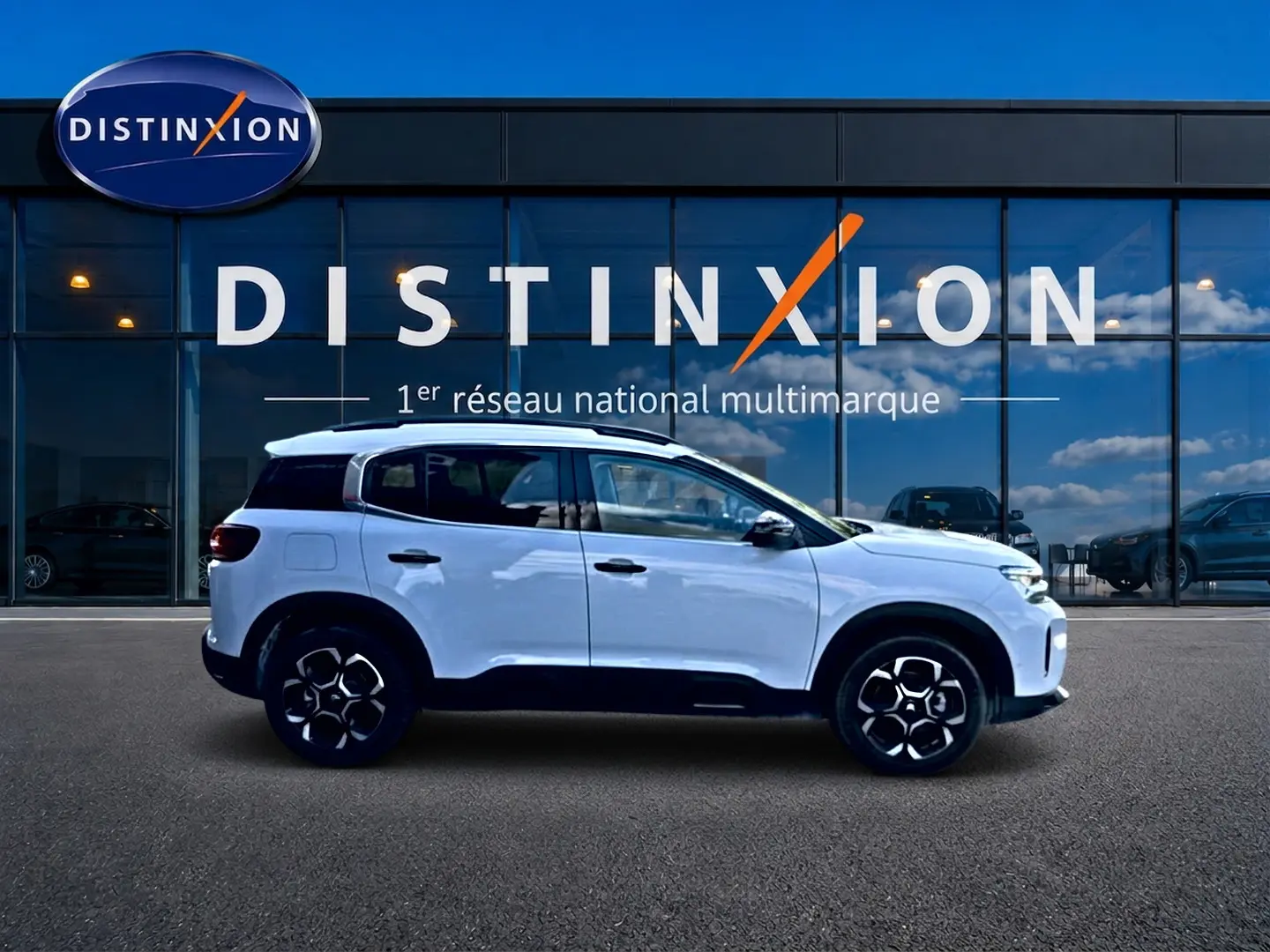 Profil droit d'un Citroën C5 Aircross blanc 2025 avec jantes alu et barres de toit devant une vitrine Distinxion.
