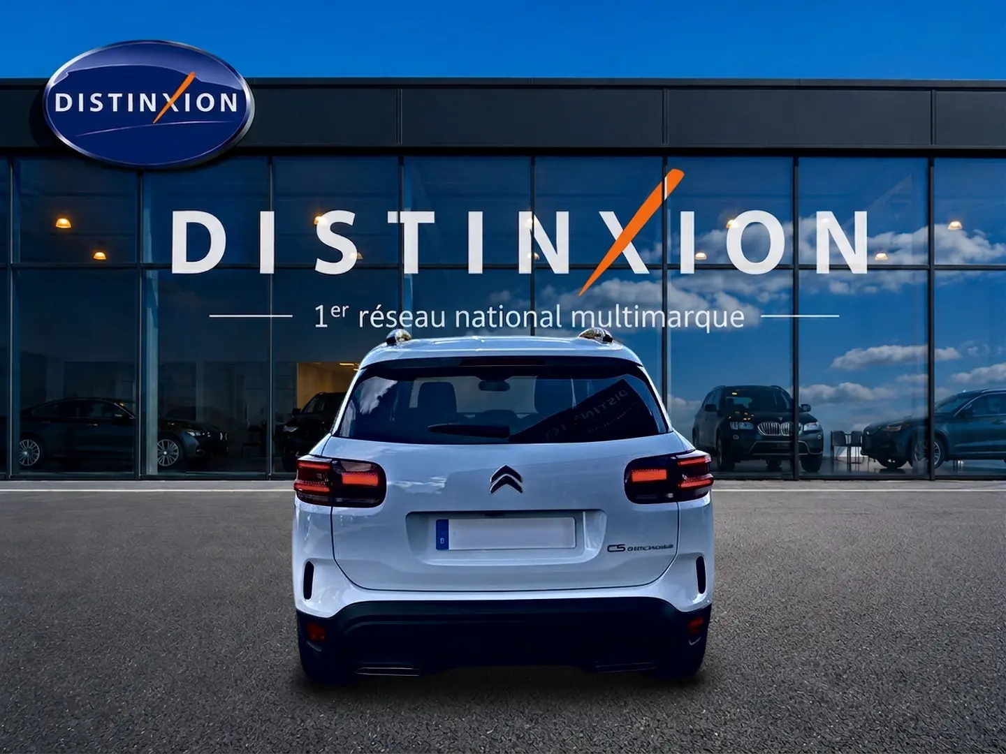 Vue arrière d'un Citroën C5 Aircross blanc 2025 stationné devant une vitrine avec logo Distinxion.