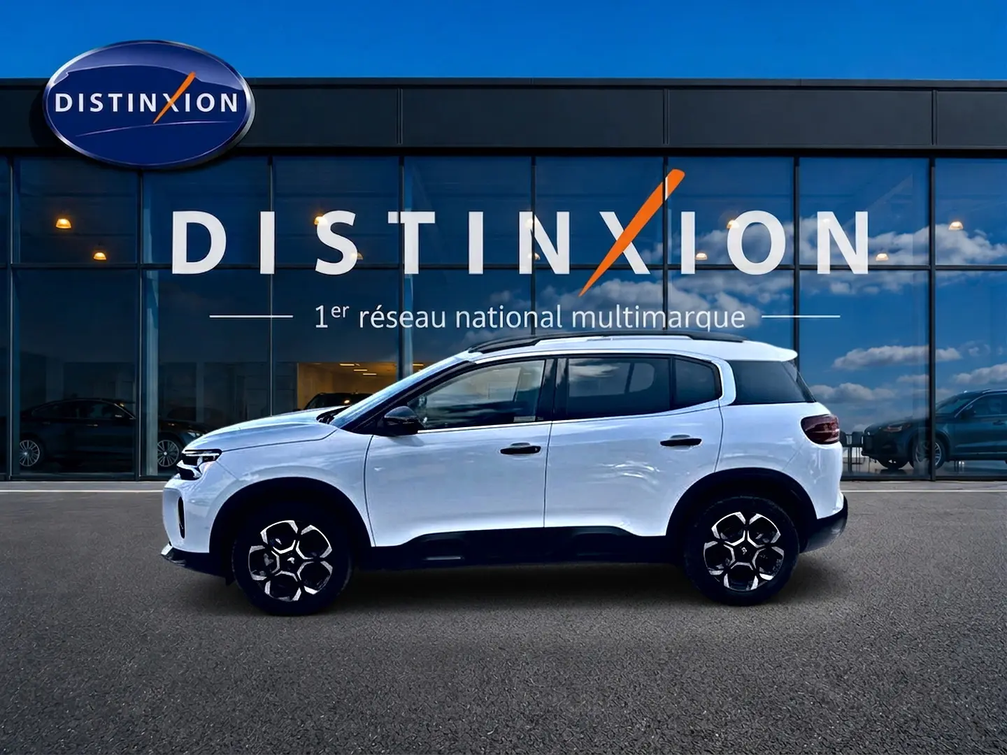 Vue de profil côté gauche d'un Citroën C5 Aircross blanc 2025 devant une vitrine avec logo Distinxion.