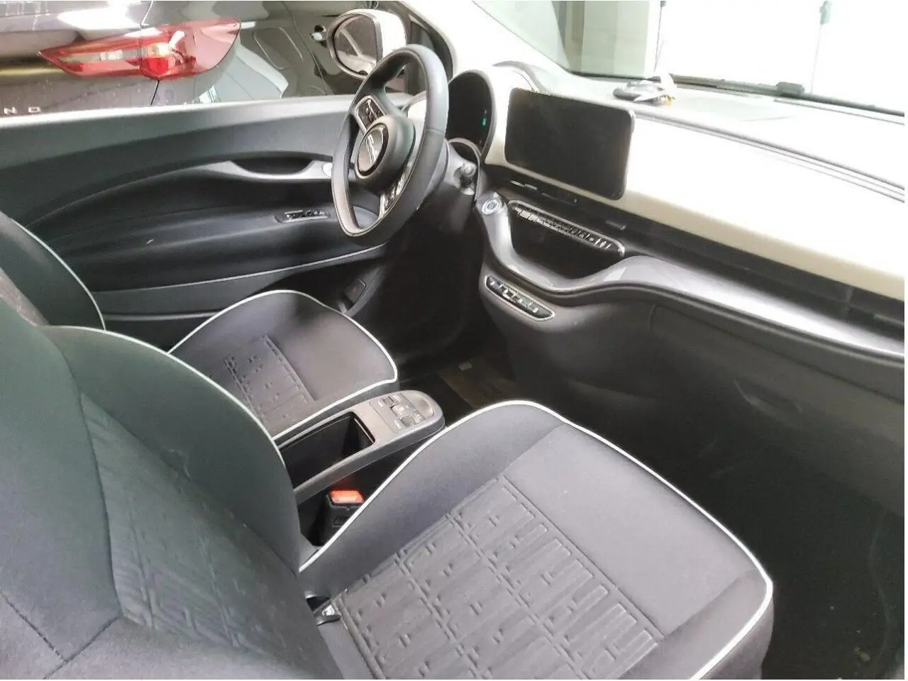 Intérieur de la Fiat 500 électrique 2024 vu côté conducteur, avec tableau de bord clair et sièges noirs à surpiqûres blanches.