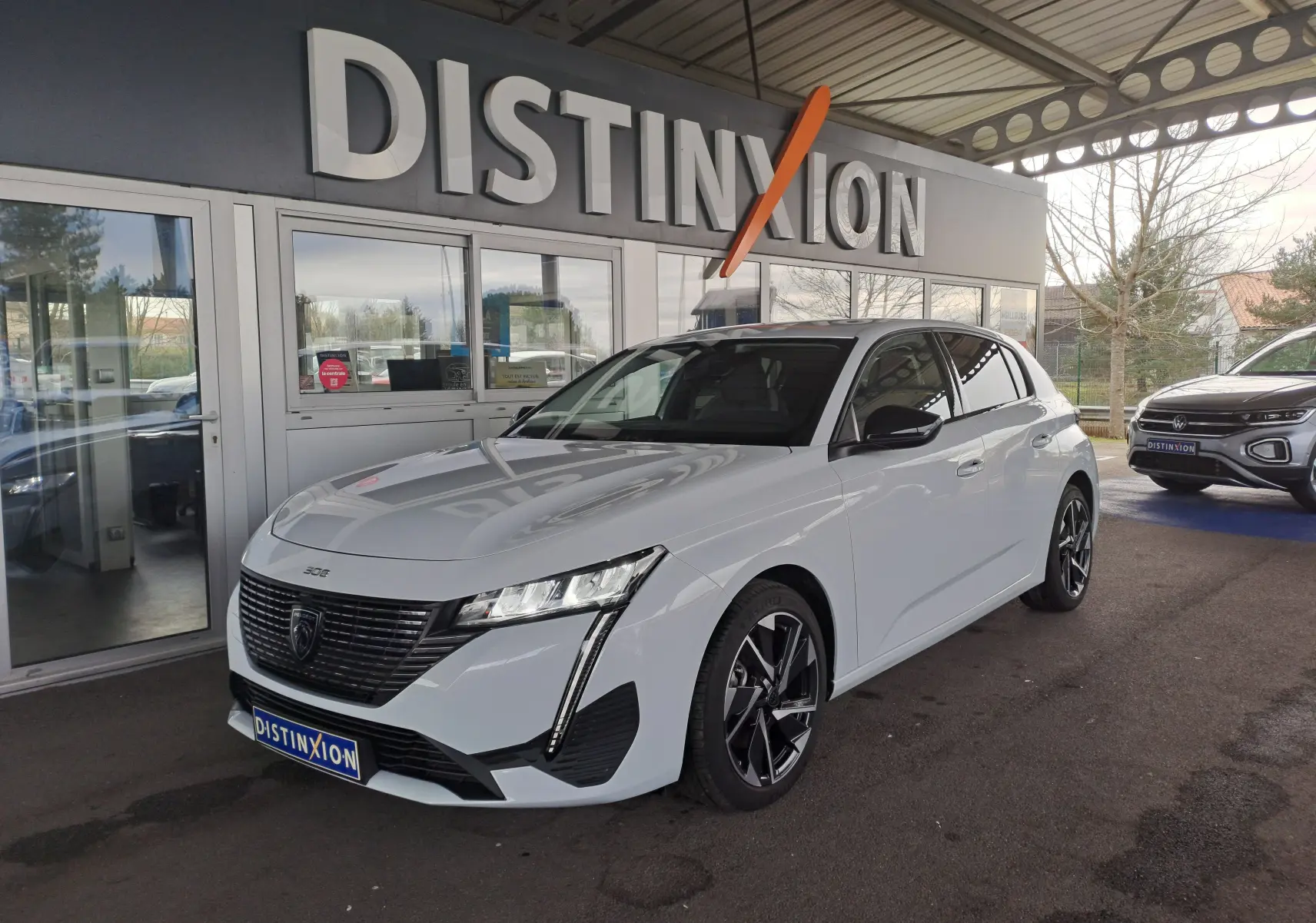 Peugeot 308 blanc Okenite vue 3/4 avant droit, avec calandre noire et jantes alliage noires au showroom Distinxion.