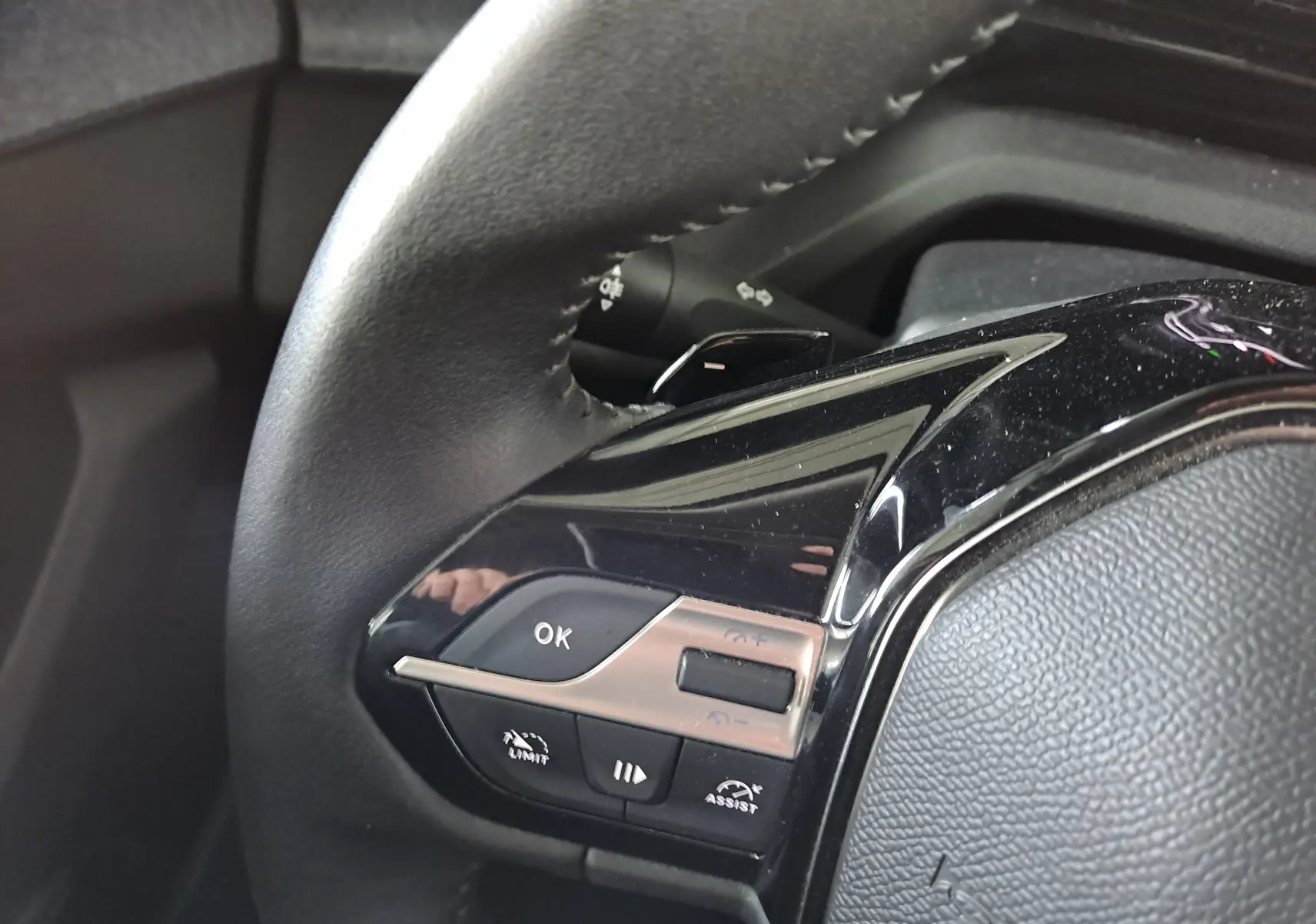 Gros plan sur les commandes gauche du volant noir du Peugeot 308 blanc Okenite 2024 avec boutons multifonctions.