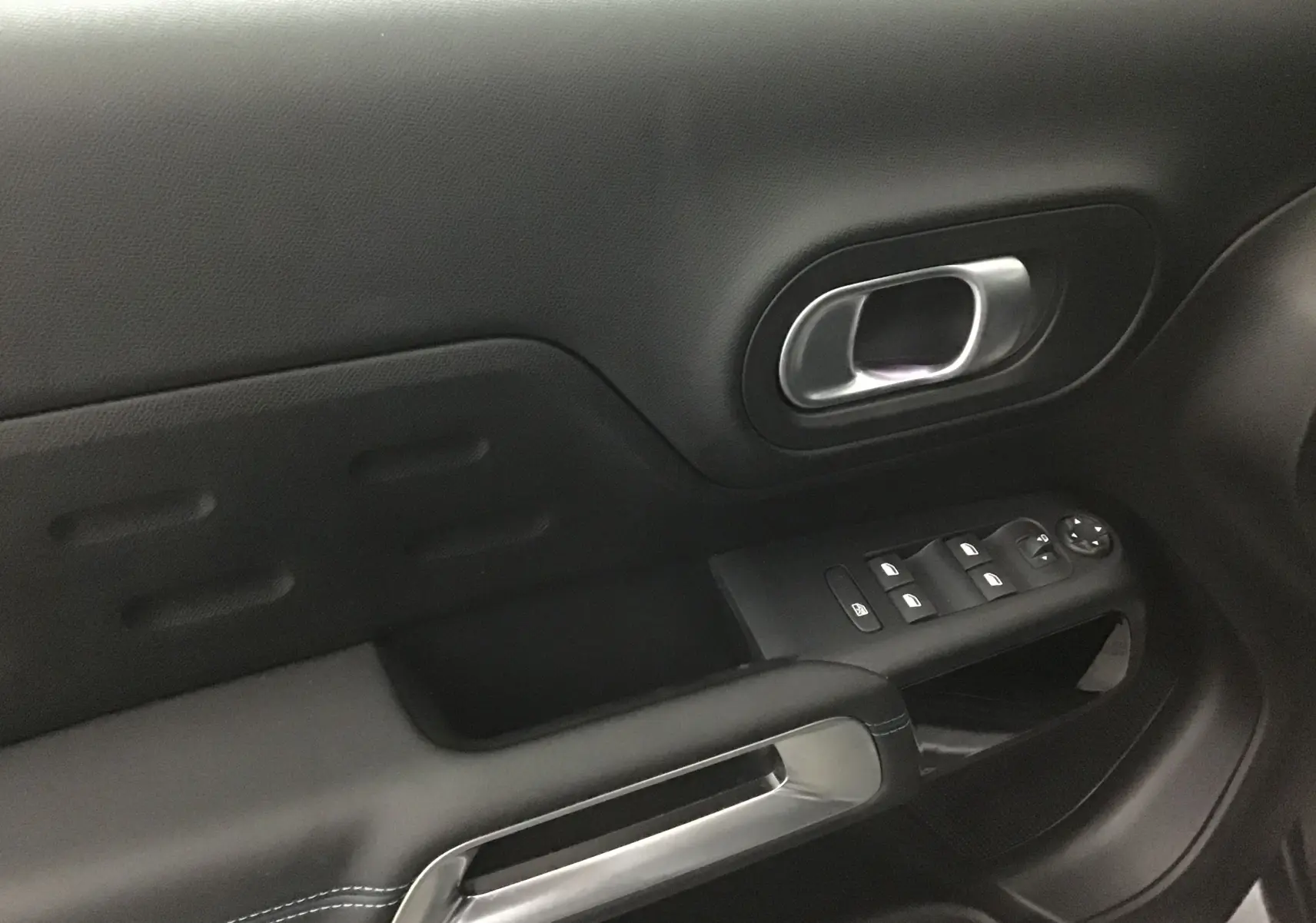 Poignée intérieure et commandes de lève-vitres côté gauche en plastique noir et métal dans un Citroën C5 Aircross 2024 gris artense.