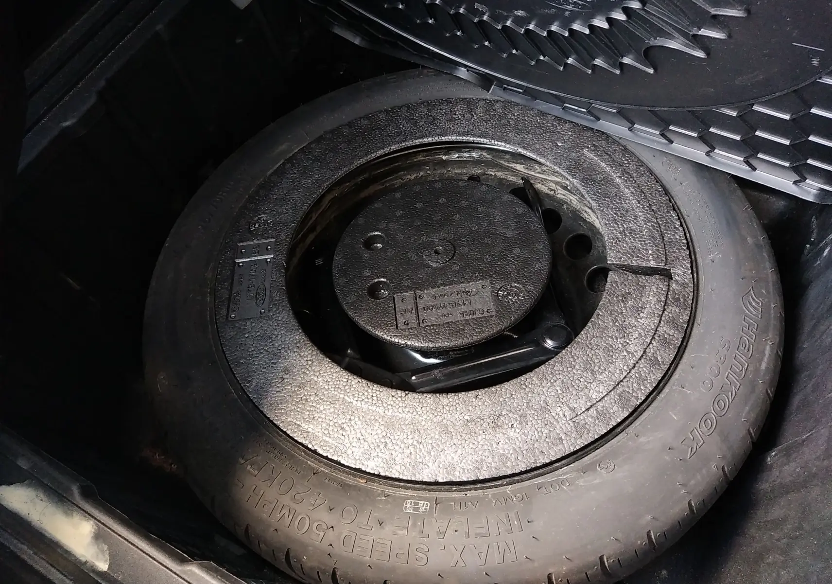 Gros plan sur la roue de secours et le rangement sous le coffre d'une Ford Puma blanche, version hybride essence 2021.