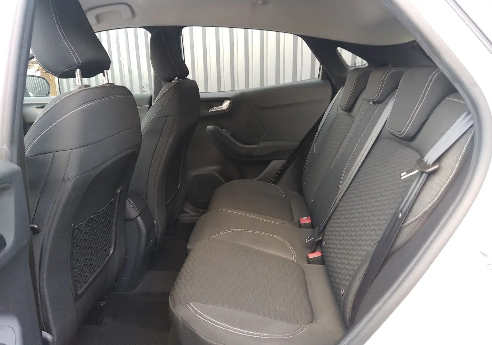 Vue intérieure côté gauche des sièges arrière noirs avec surpiqûres blanches d'un Ford Puma blanc 2021 hybride essence.