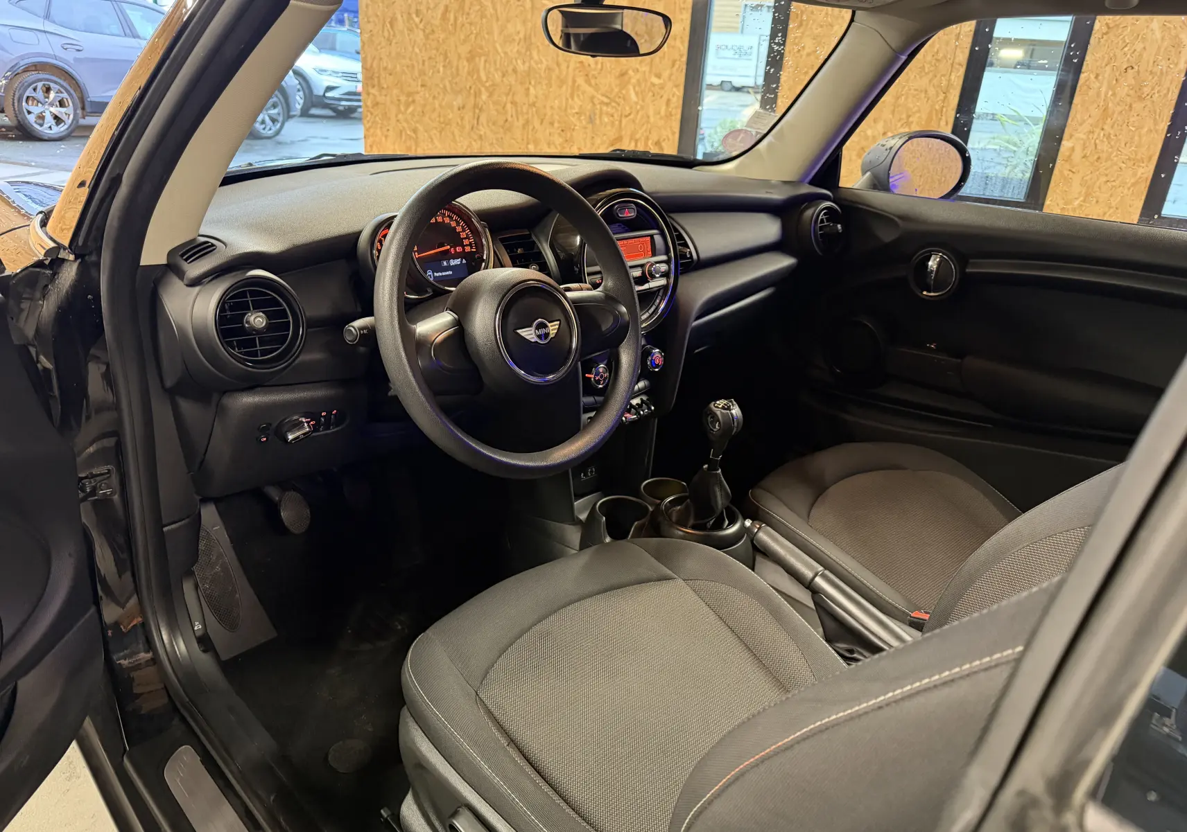 Intérieur noir de MINI 1.5i 75CV ONE 2018 vu côté conducteur, avec volant, tableau de bord et levier de vitesse manuel.