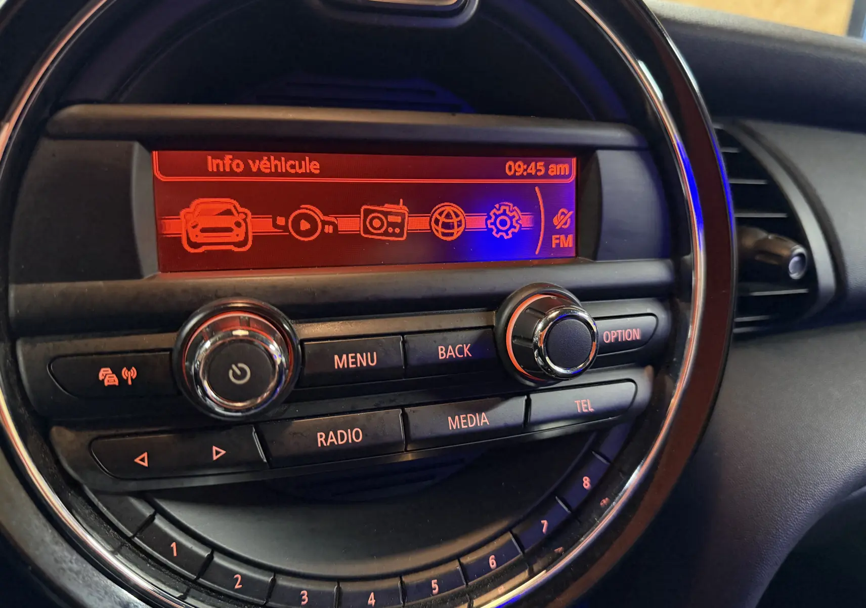 Vue rapprochée du tableau de bord de la MINI noire, affichant l'écran central rouge avec menu "Info véhicule" et commandes radio.