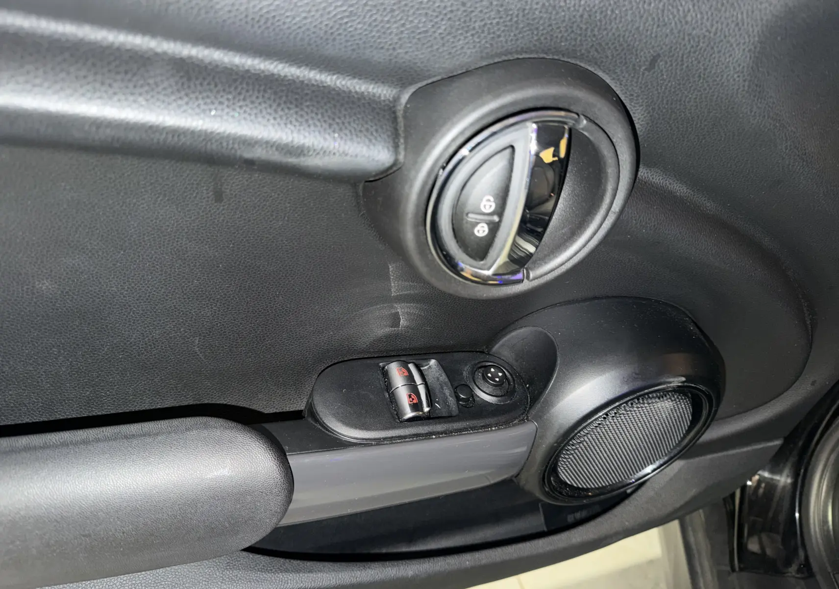 Détail de la porte intérieure côté conducteur d’une MINI noire, avec commandes électriques des vitres et poignée chromée.