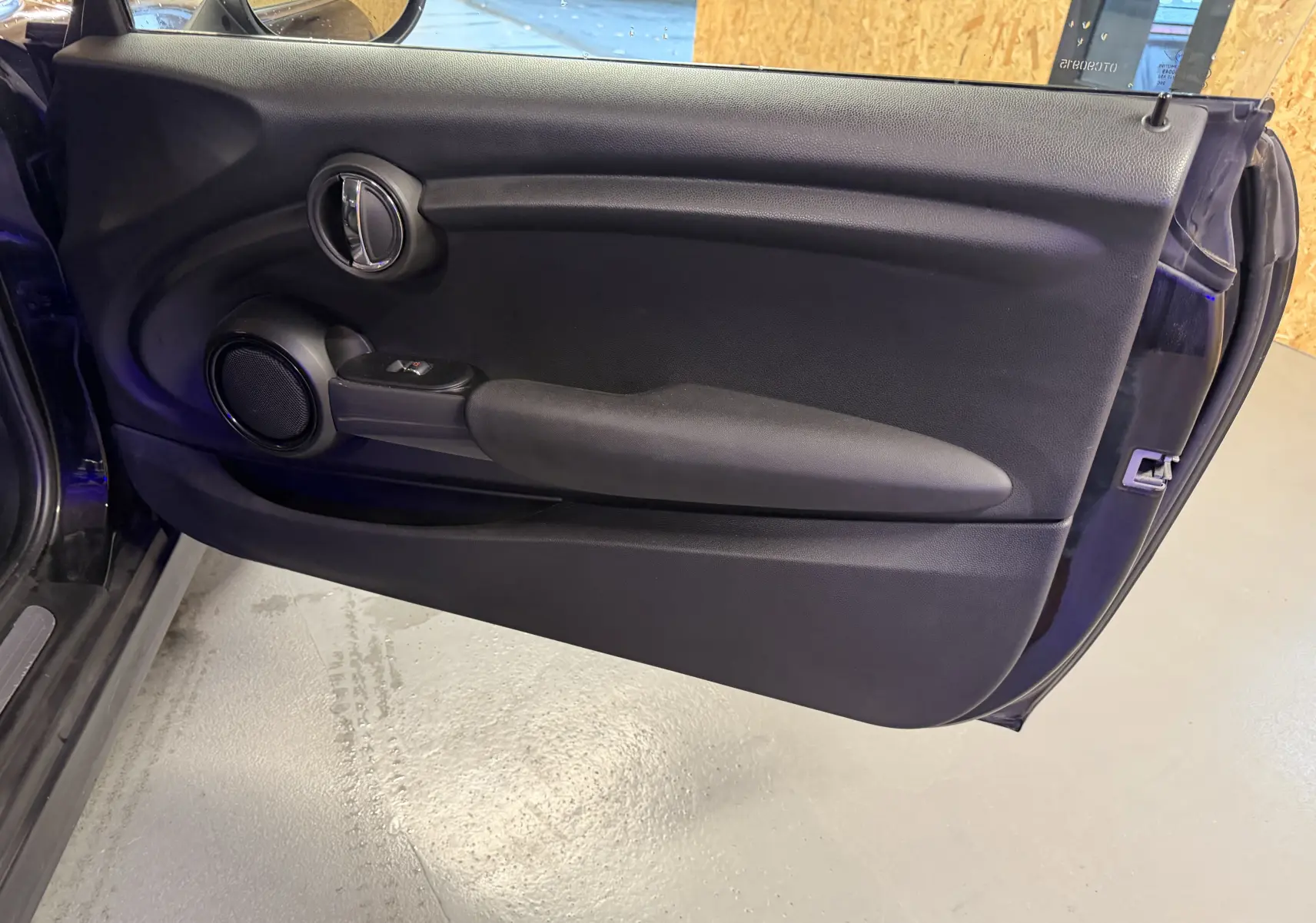 Vue intérieure de la porte côté gauche noire d'une MINI 1.5i 75CV ONE, avec commande de vitre électrique et haut-parleur intégré.