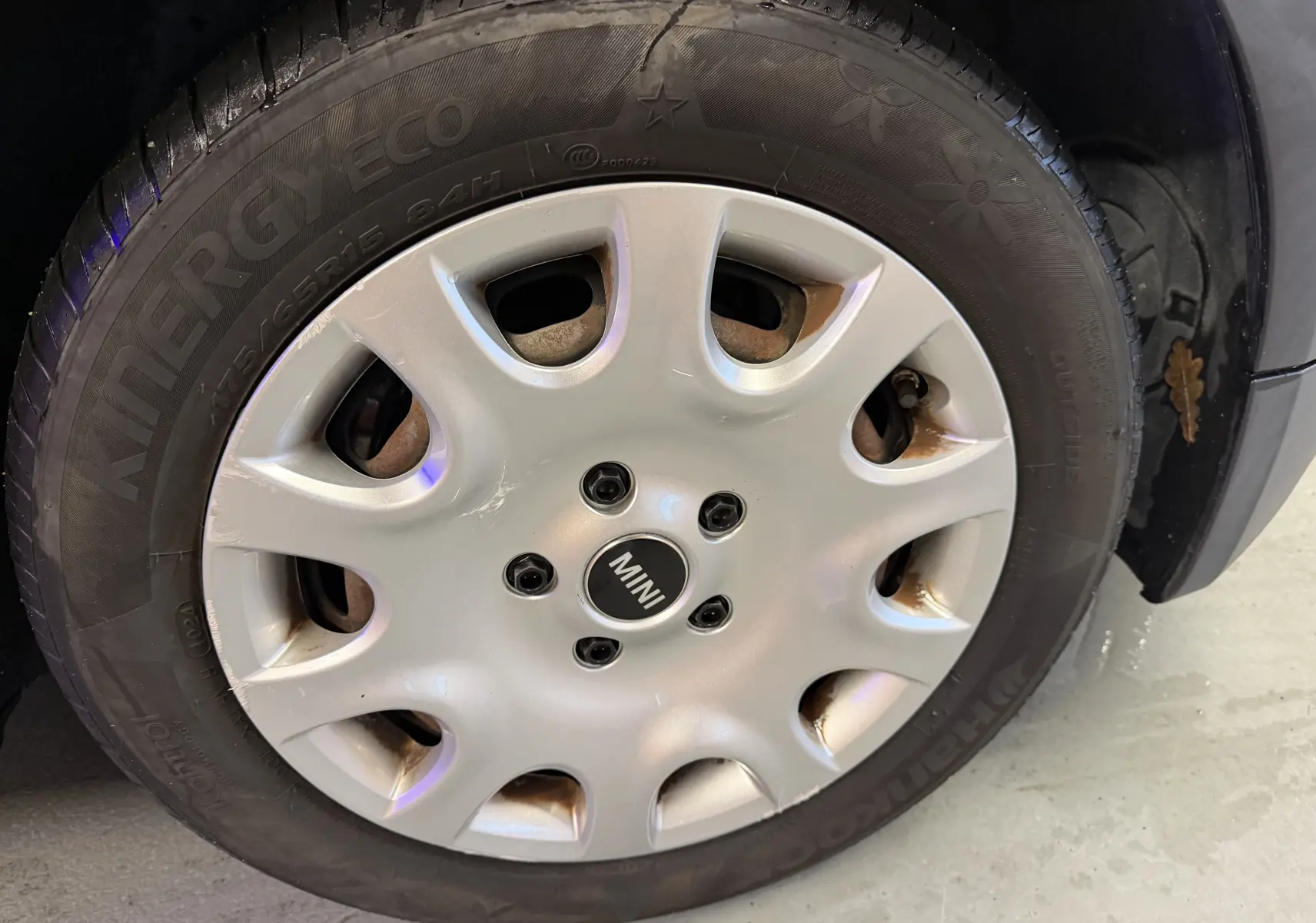 Gros plan sur la roue avant droite d'une MINI noire, mettant en valeur la jante argentée avec logo MINI au centre.