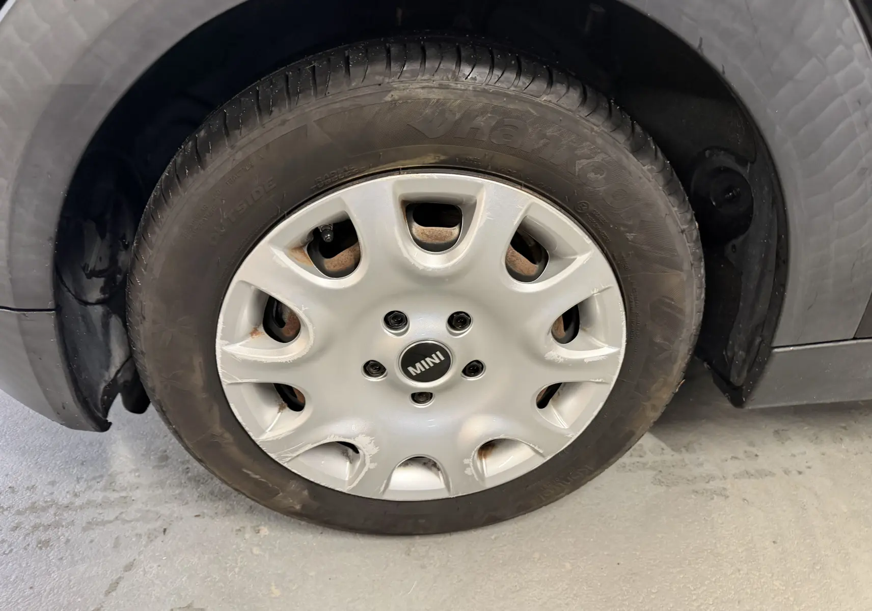 Gros plan sur la roue avant gauche d'une MINI noire, avec jante en alliage argentée et logo MINI au centre.