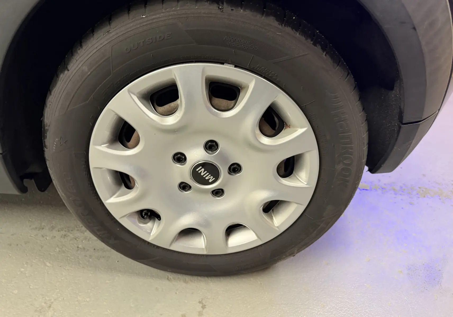 Gros plan sur la roue avant droite d’une MINI noire de 2018 avec jante en alliage argenté et logo MINI au centre.