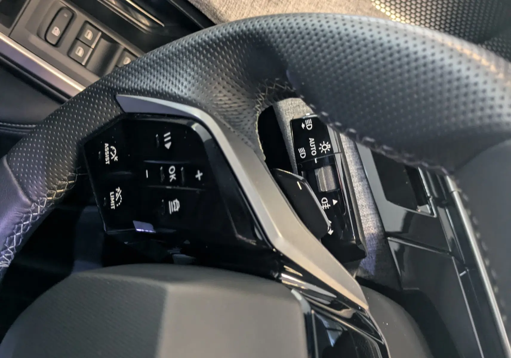 Gros plan sur le volant multifonction en cuir perforé et la portière côté gauche avec tissu gris du Peugeot 5008 Hybrid 2025.