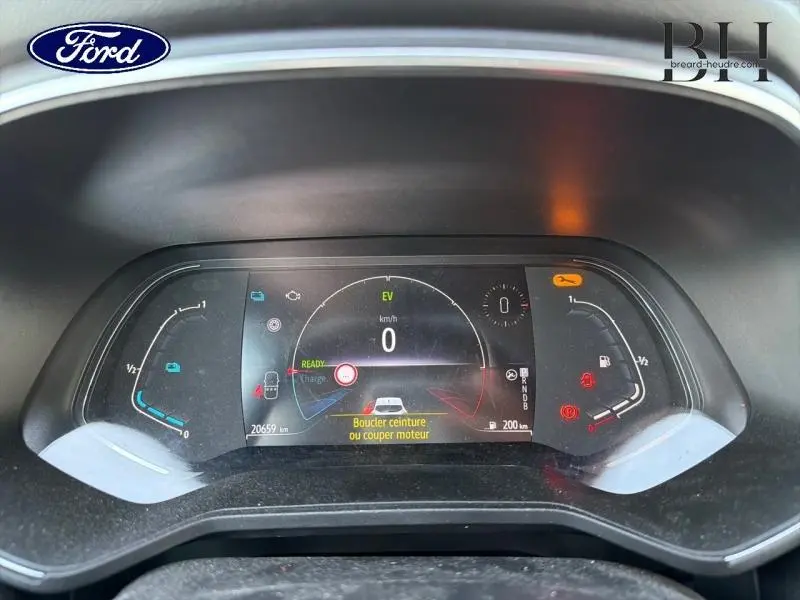 Vue rapprochée du tableau de bord numérique d'une Renault Clio blanche, affichant les alertes et informations de conduite.