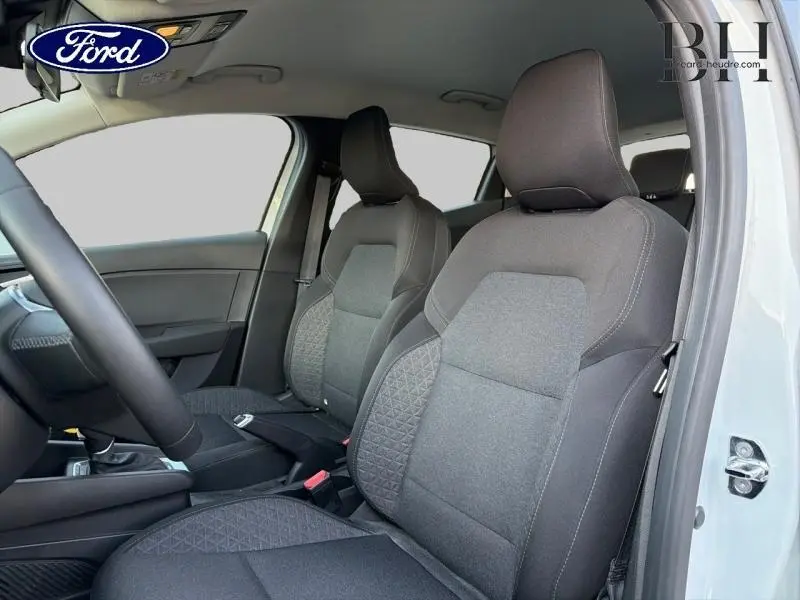 Vue intérieure côté conducteur de la Renault Clio blanche, sièges avant en tissu noir avec motifs surpiqués.