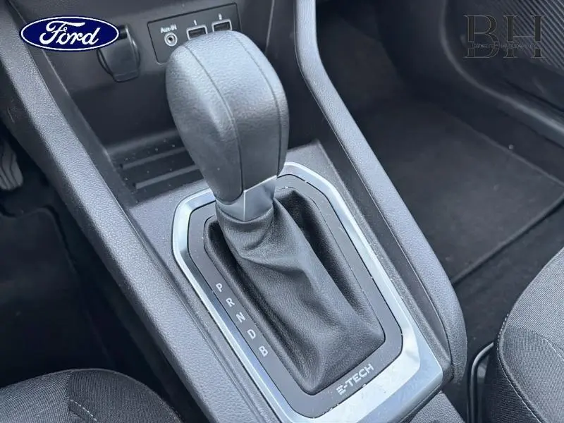 Gros plan sur la commande de boîte automatique noire avec soufflet cuir, intérieur sombre d'une Renault Clio blanche hybride.