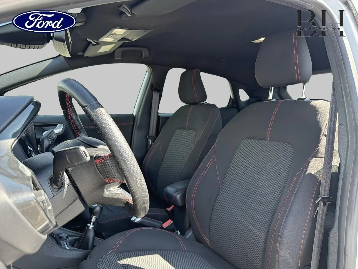 Vue intérieure côté conducteur du Ford Puma 2023, sièges noirs avec surpiqûres rouges et volant sport multifonction.