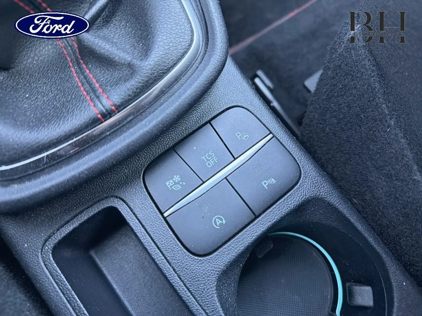 Gros plan sur la console centrale noire du Ford Puma 2023, avec boutons de contrôle et surpiqûres rouges visibles.