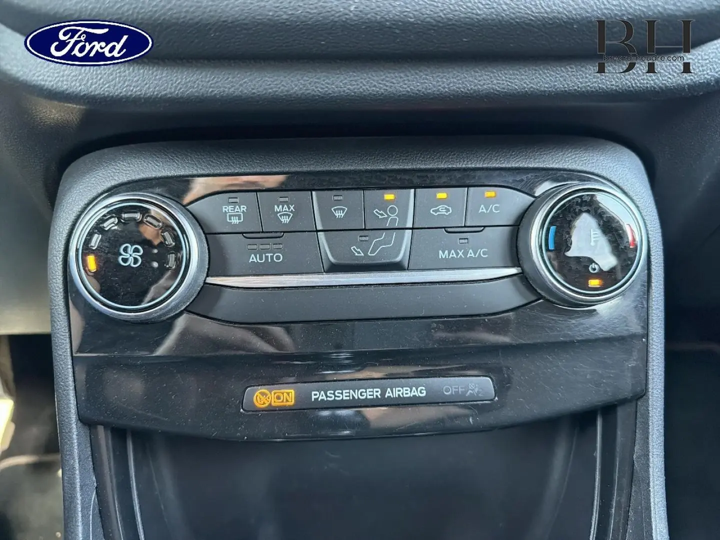 Vue rapprochée du tableau de bord noir du Ford Puma 2023 montrant les commandes de climatisation et l'indicateur airbag passager activé.