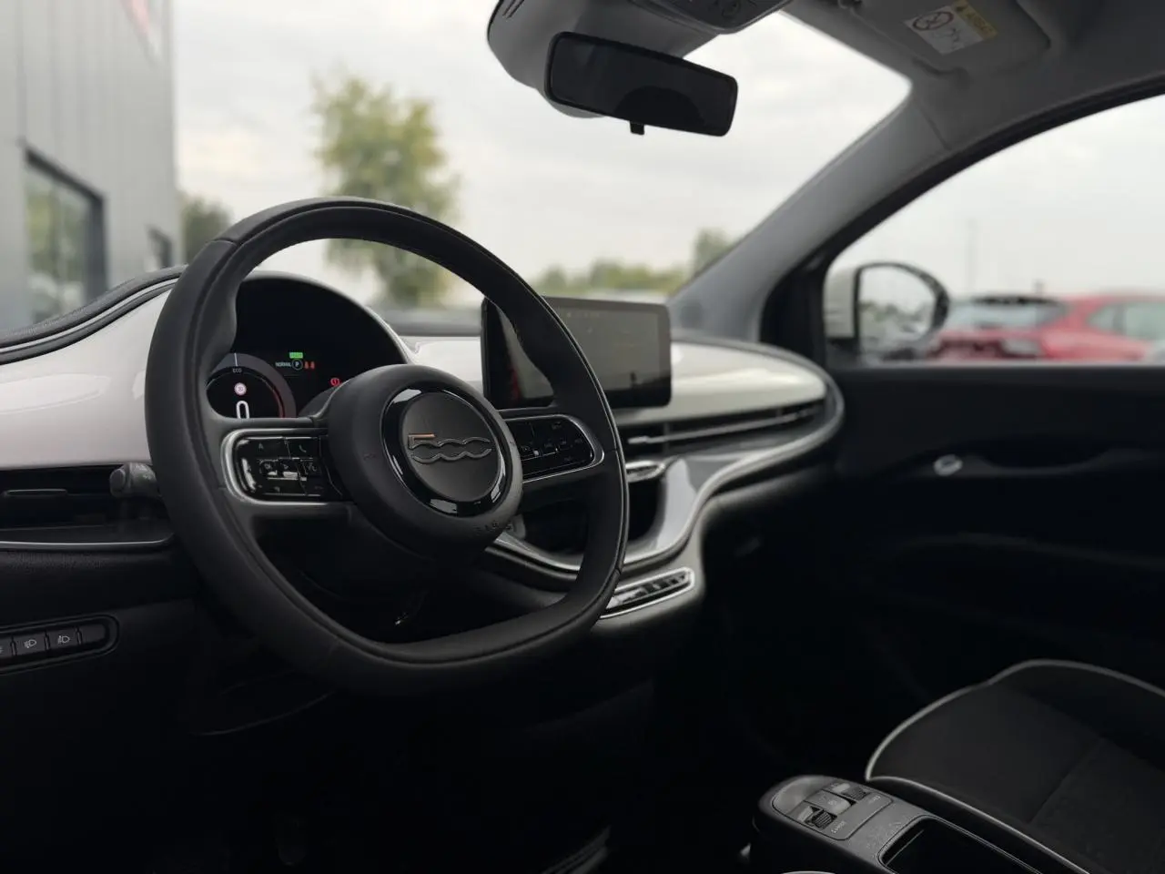 Vue intérieure avant droite de la Fiat 500 électrique 2024, tableau de bord blanc avec écran tactile et volant noir.