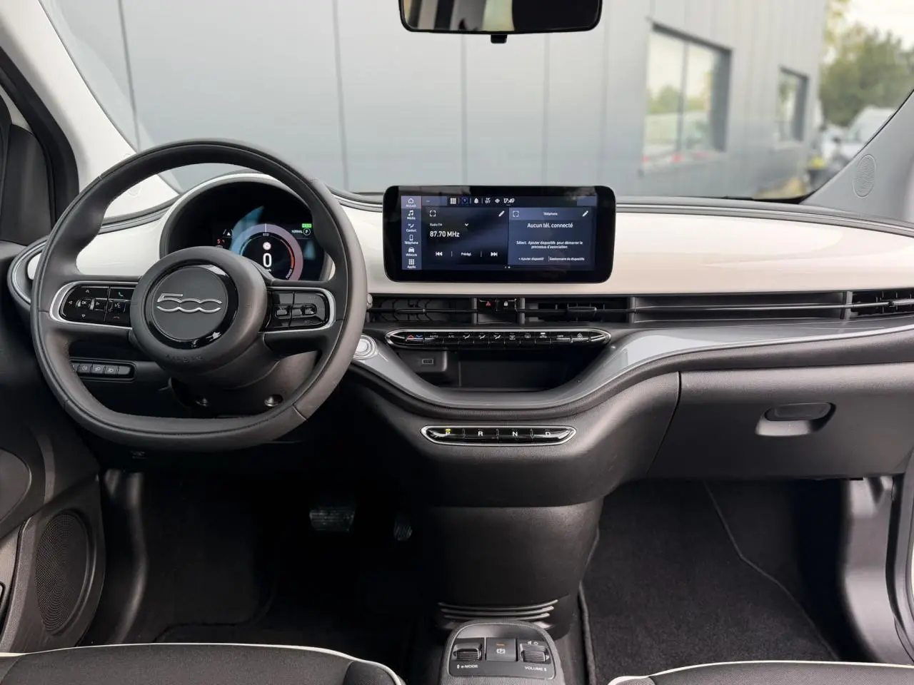 Vue intérieure avant du tableau de bord blanc et noir de la Fiat 500 électrique 2024 avec écran tactile central et volant multifonction.