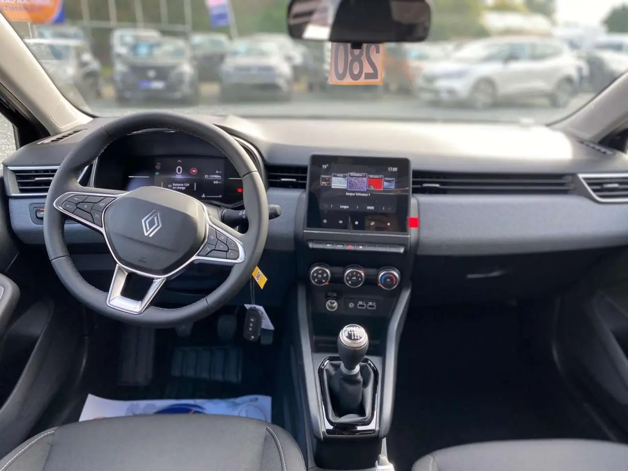 Vue intérieure avant de la Renault Clio Evolution 2025 avec volant multifonction, écran tactile et levier de vitesse manuel.