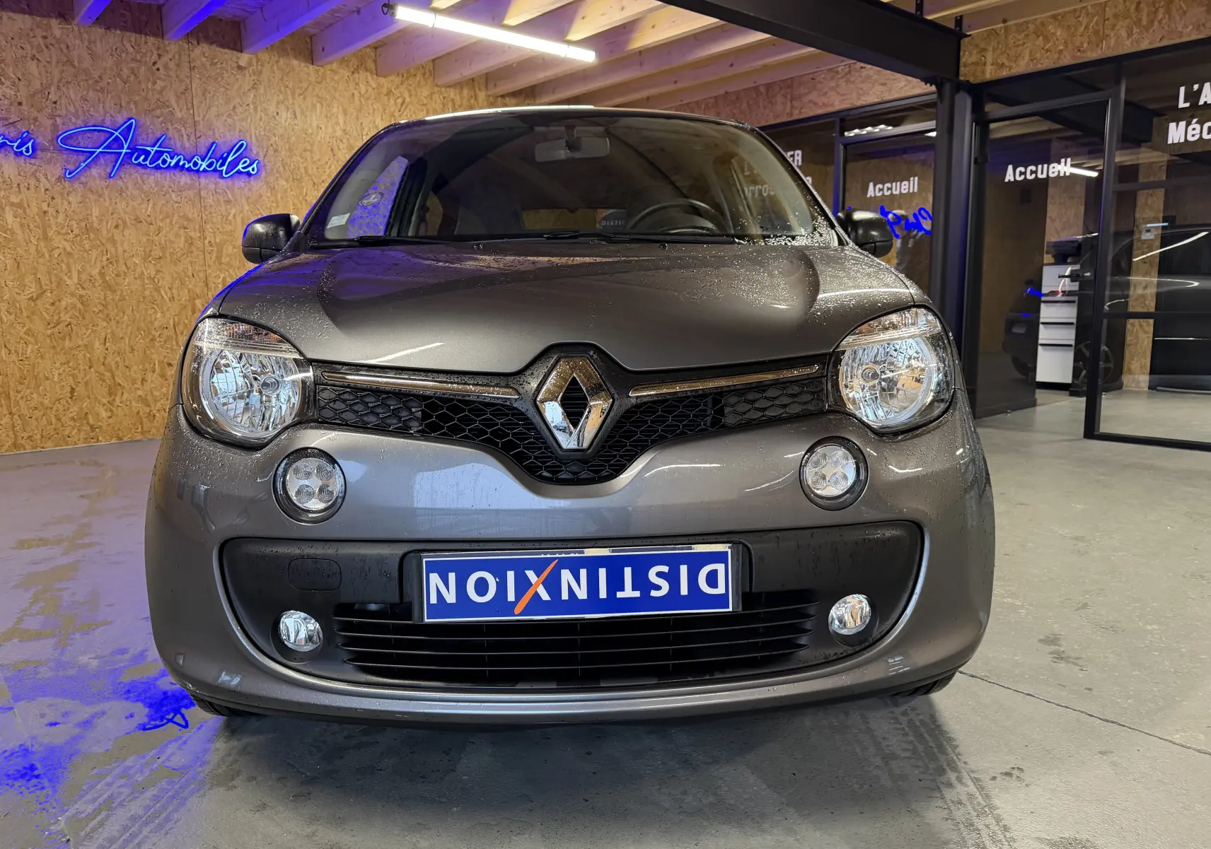 Vue de face d'une Renault Twingo III gris métallisé, avec phares halogènes et antibrouillards visibles en intérieur showroom.