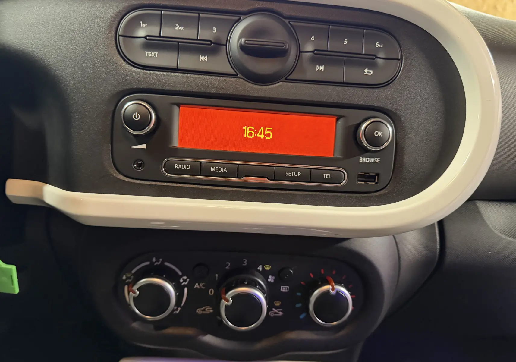 Gros plan sur la console centrale de la Renault Twingo III gris, affichage radio orange et commandes climatisation manuelle.