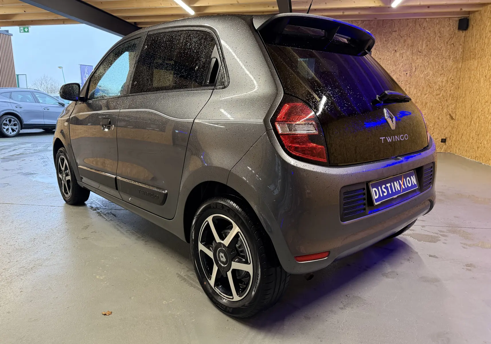 Vue 3/4 arrière droite d'une Renault Twingo III gris métallisé avec jantes alliage et vitres teintées, stationnée en intérieur.