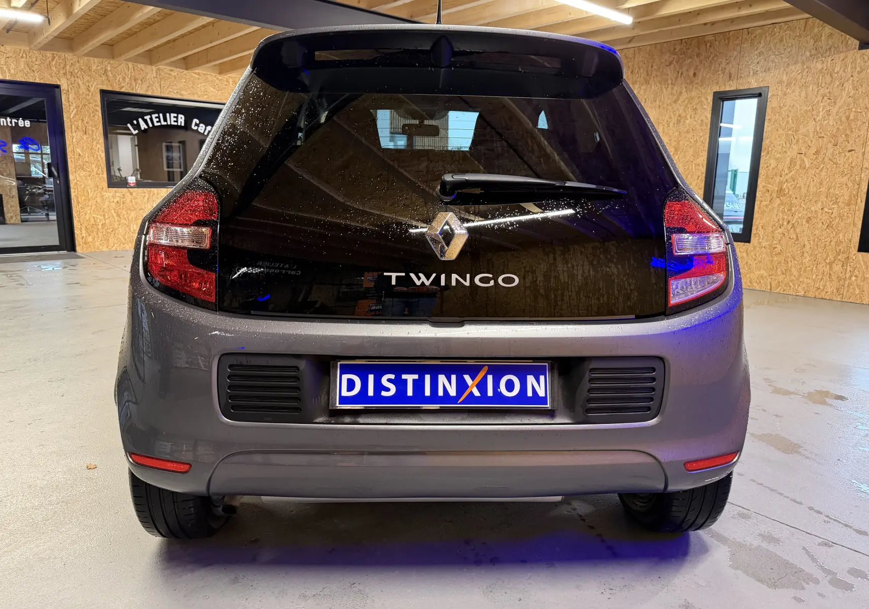 Vue arrière d'une Renault Twingo III gris métallisé avec vitre arrière noire et feux rouges allongés.