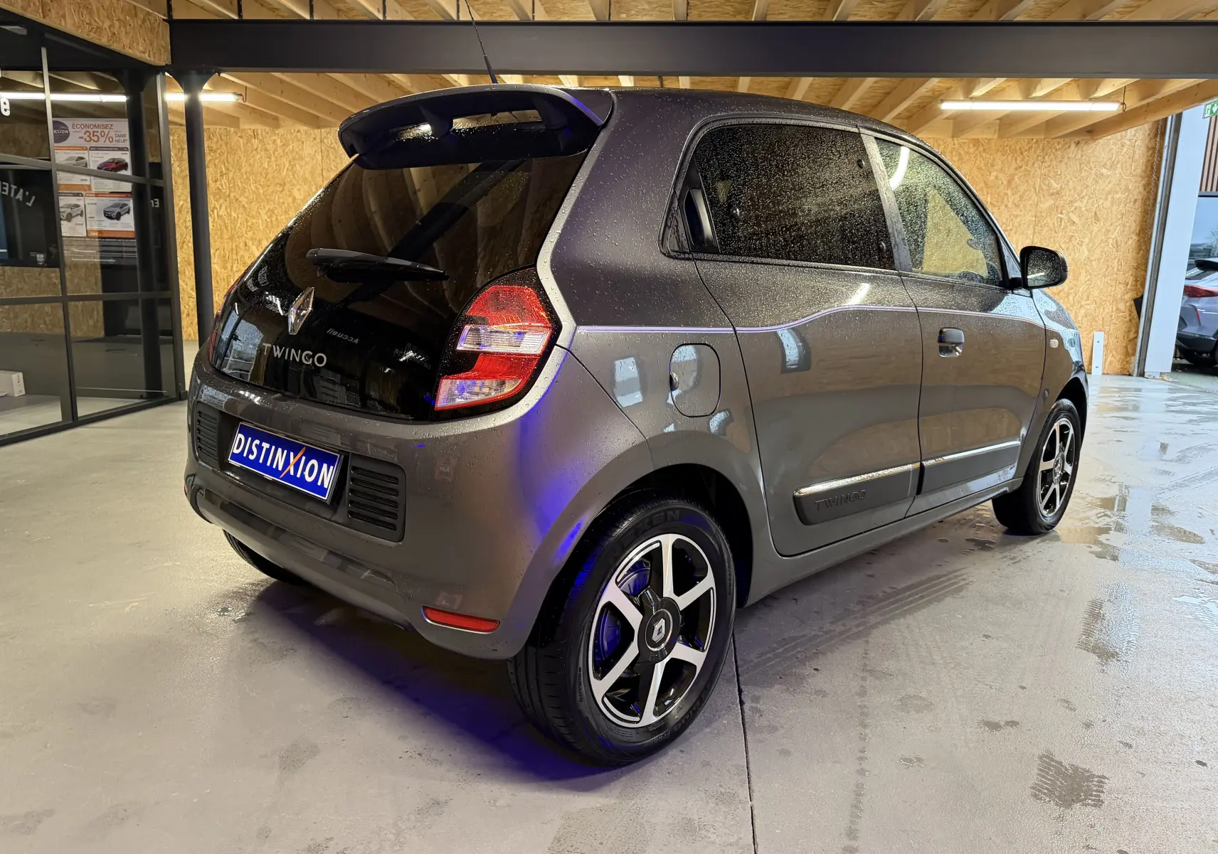 Renault Twingo III gris vue 3/4 arrière droit, avec jantes alliage et vitres teintées en intérieur d'atelier.