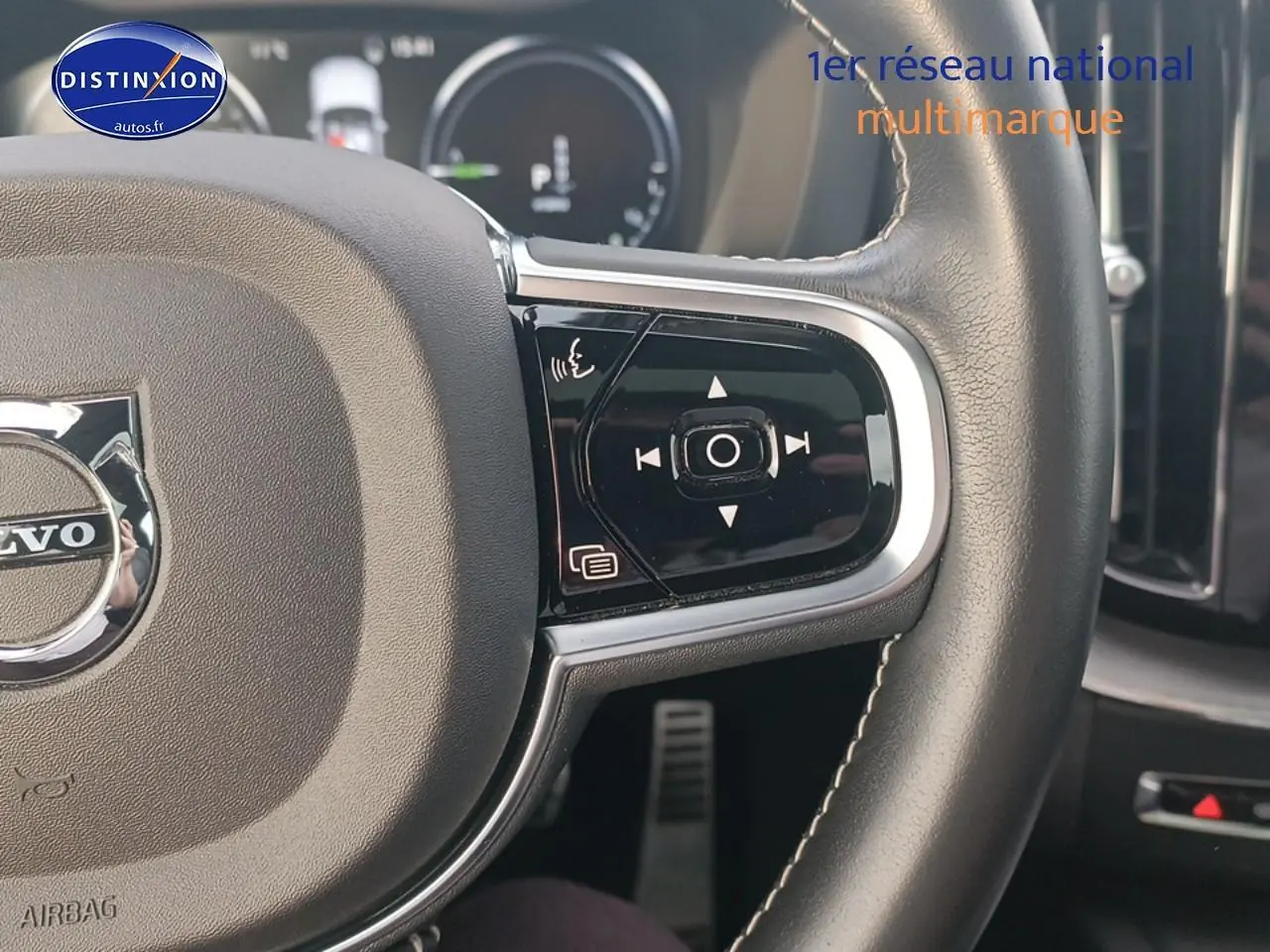 Gros plan sur le volant cuir noir multifonction du Volvo XC60 blanc, avec commandes intégrées et logo central visible.
