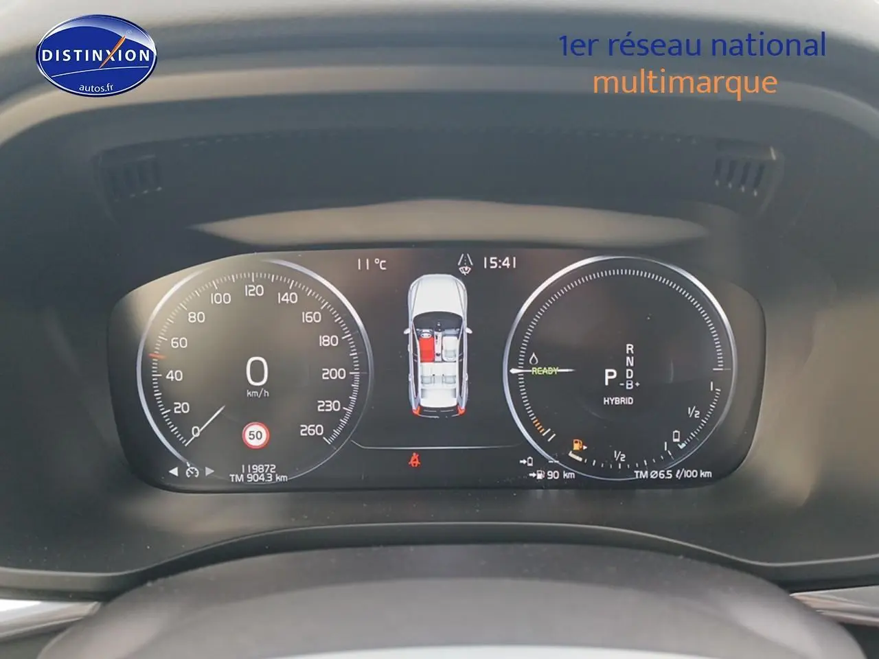 Tableau de bord numérique du Volvo XC60 blanc, affichant vitesse, mode hybride et état des portes ouvertes.