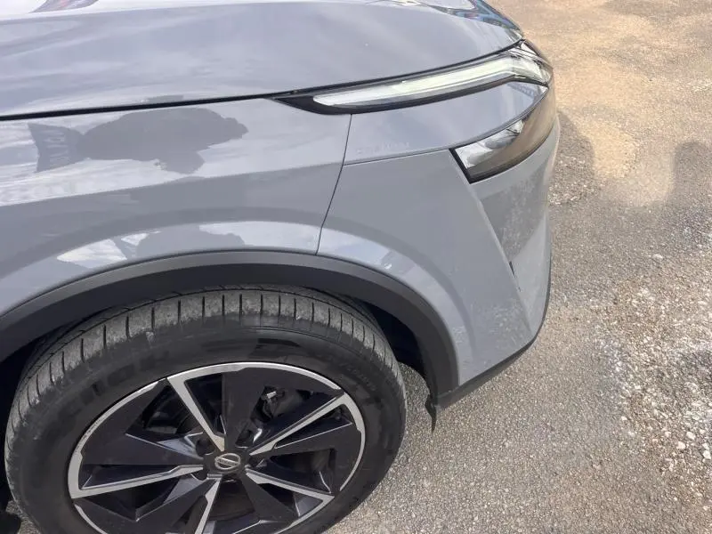 Gros plan sur l'aile avant droite gris argile du Nissan Qashqai 2022 avec jante alliage noire et phares LED fins.