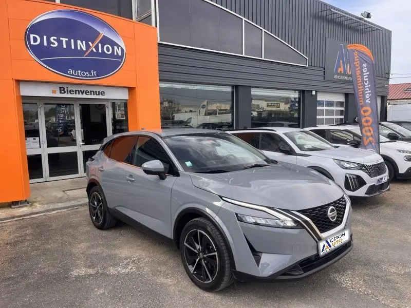 Nissan Qashqai 1.3 Mild Hybrid gris argile avec toit noir, vue 3/4 avant droit devant un concessionnaire.