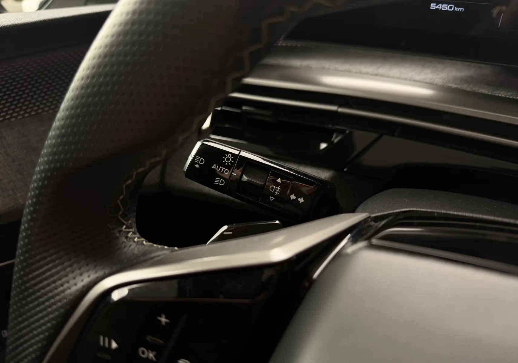 Gros plan sur la commande des feux et clignotants à gauche du volant dans l’habitacle du Peugeot 5008 Hybrid 145 e-DCS6 GT.