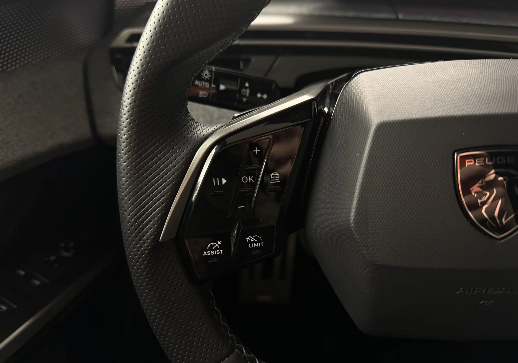 Gros plan sur le volant cuir perforé côté gauche du Peugeot 5008 Hybrid 145 e-DCS6 GT avec commandes intégrées.