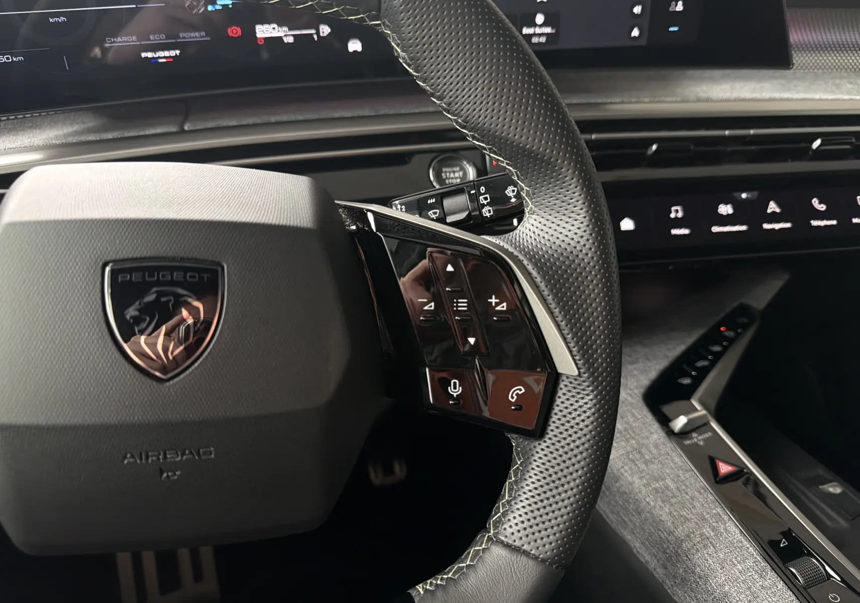 Gros plan sur le volant perforé et les commandes tactiles du Peugeot 5008 Hybrid 145 e-DCS6 GT 2025, intérieur moderne noir.