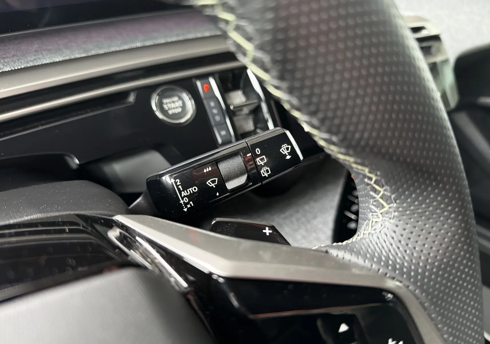 Gros plan sur la commande d’essuie-glace à gauche du volant perforé dans l’habitacle du Peugeot 5008 Hybrid blanc.
