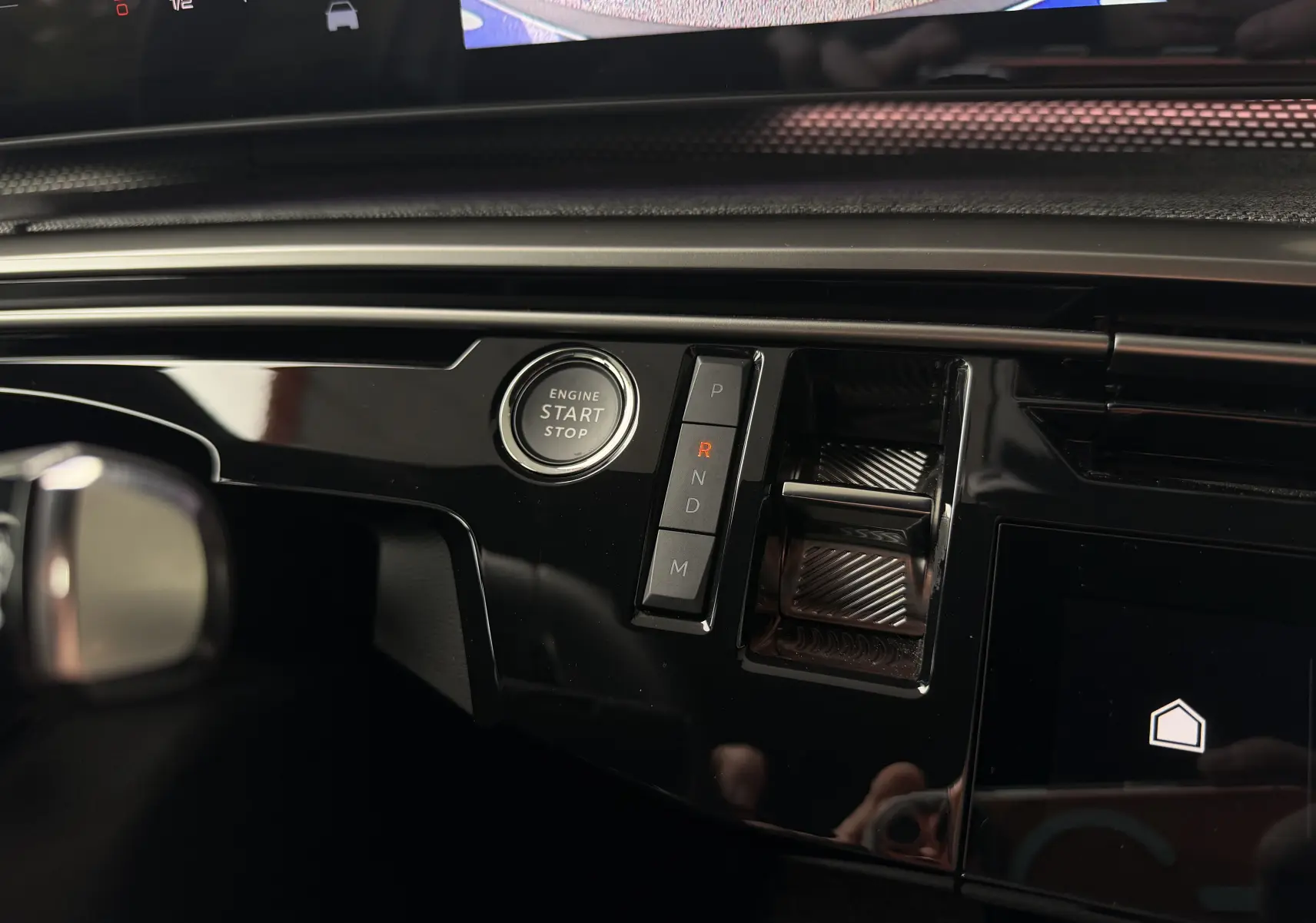 Gros plan sur la console centrale noire brillante du Peugeot 5008 Hybrid 145 e-DCS6 GT avec bouton start/stop et commandes de boîte auto.