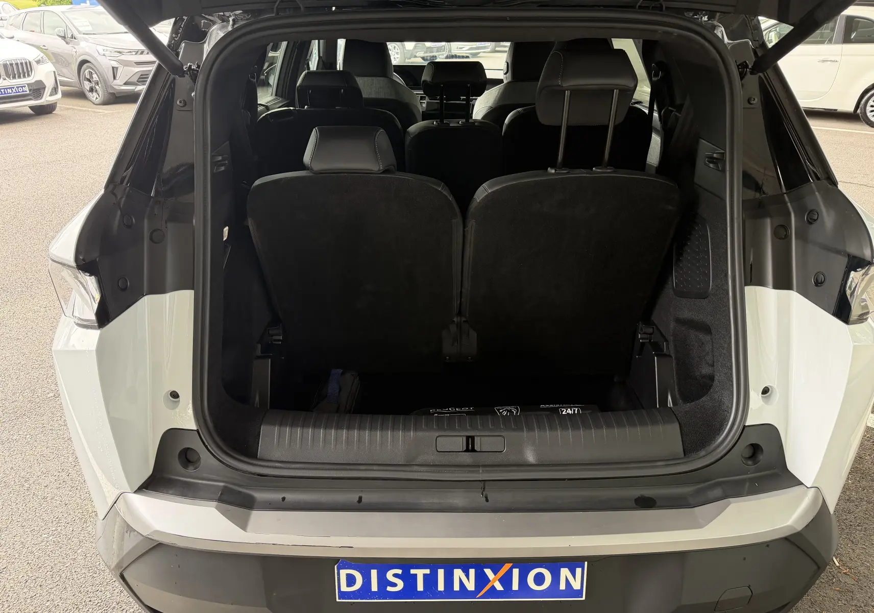 Vue arrière du coffre ouvert d’un Peugeot 5008 Hybrid blanc Okenite avec toit noir, montrant les sièges arrière relevés.